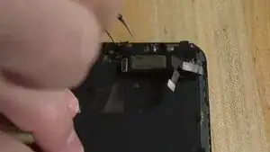 After taking out all four screws, gently fold the proximity sensor to prevent strain on the ribbon. Warm the top of the screen with the iOpener for 15–20 seconds to loosen the adhesive. Once ready, carefully lift the sensor from its spot. Be very careful, as even a slight tear in the ribbon can permanently disable Face ID.