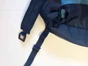Hold the duck bill clip behind the open square piece at the base of the backpack strap