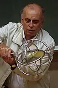 Dieser Mann hält einen drehenden Kreisel fest, der kardanisch aufgehängt ist. Egal wie der Mann den Griff bewegt, die Drehachse des Kreisels behält immer die gleiche Richtung.
