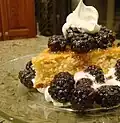 Ein Kuchenstück mit gezuckerten Brombeeren und Schlagsahne