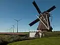 Vorne sieht man eine alte Windpumpe, hinten eine moderne Windkraftanlage.