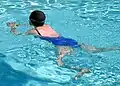 Eine Frau im Badeanzug und mit Badekappe schwimmt im Pool.