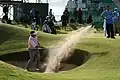 Ein Golfer schlägt seinen Ball aus dem Bunker. Das ist beim Golf eine Fläche mit Sand.