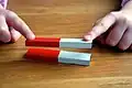 Der obere Magnet „schwebt“, weil sich die roten und weißen Pole jeweils abstoßen.