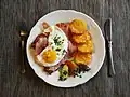 Ein Schnitzel, versteckt unter Speck und Spiegelei, mit Röstini, runden Rösti-Scheiben