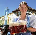 Eine Kellnerin im Dirndl mit Maßkrügen. Eine Maß ist ein Liter Bier.