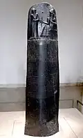 Ein großer Stein mit den Gesetzen des Hammurabi. Darüber steht der König vor einem sitzenden Gott.
