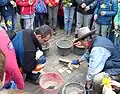 Kinder sehen Gunter Demnig beim Verlegen der Stolpersteine zu. Sie haben Blumen mitgebracht.