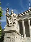 In Athen gibt es heute wieder eine Akademie. Davor steht eine Statue von Platon. Die Figur dahinter ist die Göttin Athene.
