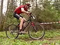 Dieser Fahrer fährt einen Gelände-Rundkurs auf einem Mountainbike. Der Sport heißt „Cross Country”, also querfeldein.