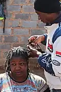 Ein Hairstylist in Johannesburg, in Südafrika, macht der Kundin Dreadlocks.