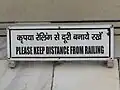 Schild auf Hindi und Englisch: Man soll Abstand vom Geländer oder der Reling halten.