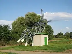 Skulptur, die einem Freileitungsmasten nachempfunden ist, der sich zum „Ausruhen hingesetzt“ hat
