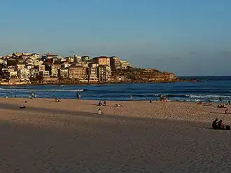 It is a beach during a sunset. There are people on the beach and buildings in the background