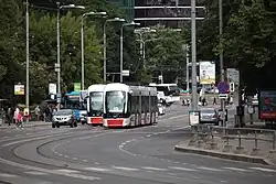 Trams and cars in a road with people walking in the sidewalk.